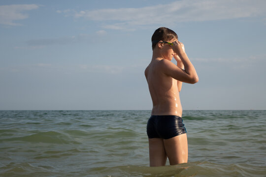 A 10-year-old boy puts on swimming goggles and prepares to swim in the sea.