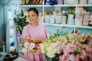 Portrait of a young beautiful caucasian woman florist in a pink dress arranging a bouquet of flowers in a flower shop