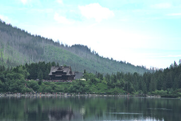 Panoramic view of the Morskie Oko mountain lake surrounding larch, pine and spruce forest with Schronisko przy Morskim Oku shelter house in background