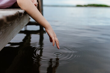 A girl dips her hand into lake water leaving ripples in concentric circles