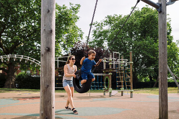 Woman swinging little boy on tire at playground