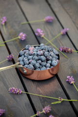 Blueberries in metal pot and lavender flowers around on a wooden table in a garden