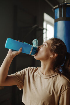young attractive girl took a break during a workout, resting and drinking water. dark boxing gym with a ring