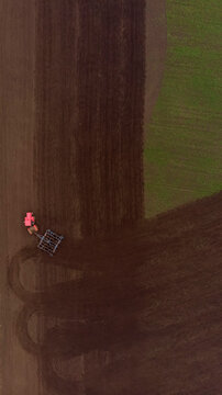 Red tractor plowing green field and and mixing earth