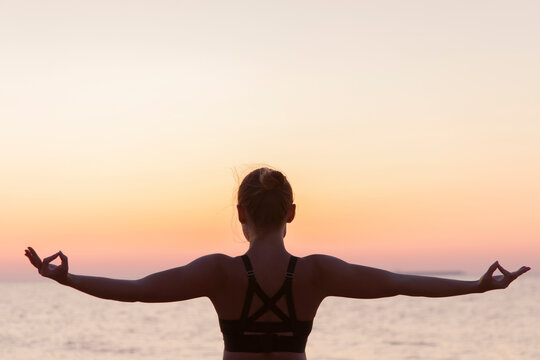 Woman contemplating ocean performing mudras with outstretched arms