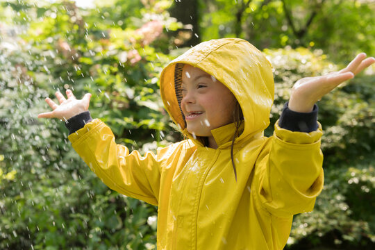 Little girl with down syndrome playing in sprinkler wearing raincoat