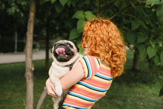 Ginger head holds her pug dog in the park