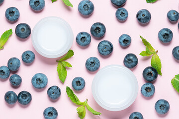 Two jars with natural moisturizing cream with blueberry extract on pink background with blueberries and mint leaves top view. Natural cosmetic concept.