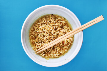 instant noodles at white bowl over blue background with copy space. fast food concept. flat lay