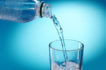 pouring fresh bottled water to glass over blue background. copy space. water flow. energy symbol conceptual