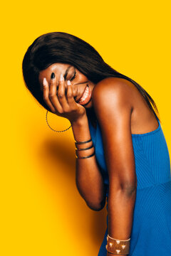 Beautiful Afro Woman posing over yellow laughing background covering her face with hand