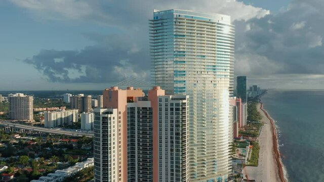 Miami, travel business and tourism industry. 4K aerial of the impressive waterfront tall white glass building. Close up aerial view on the modern residential condo and apartment building at the ocean