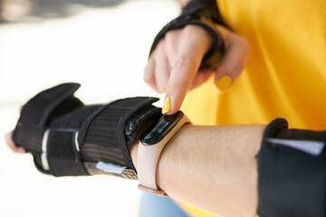 female person touching smart watch or fitness tracker while roller skating leisure activity. close up. sunny day. girl wearing hand protection for sport exercises.