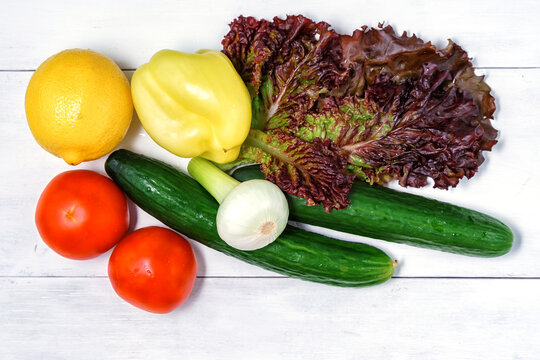 set of green vegetables on a white wooden background. tomatoes, lettuce, bell peppers, fresh onions, lemon and cucumber