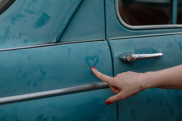 Girl draws a heart on an old car