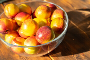 ripe juicy nectarines in a glass bowl on a wooden table on a sunny day