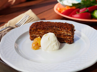 piece of cake brownie on a white plate with honey and a scoop of ice cream on the background of a plate with vegetables