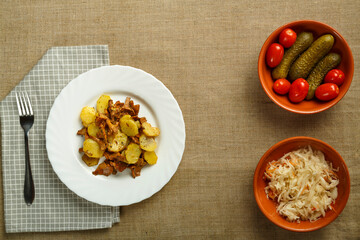a plate of potatoes with larvae mushrooms on a napkin and a fork next to pickled cucumbers and tomatoes and cabbage.