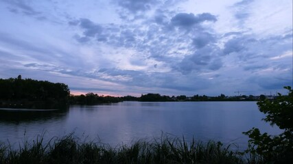 Time lapse of cumulus clouds over a Lake. Beautiful landscape with water and silhouette of vegetation. Wind in the foreground. - Powered by Adobe