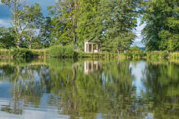 Fototapeta na wymiar A view across a beautiful lake with reflections of trees towards an old abandoned structure in the middle of a rural countryside scene