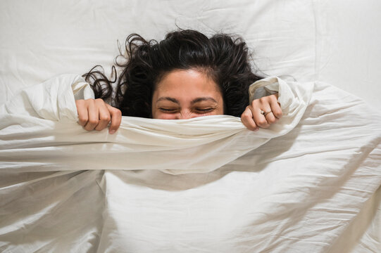 Happy young woman wrapped in white sheets in the bed