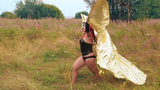 A woman in the image of a demon in a black corset with golden wings in the field.
