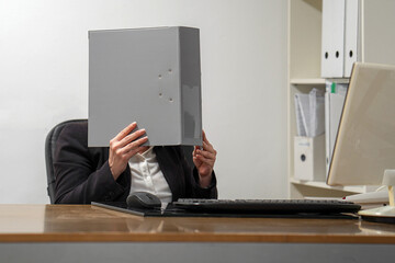 Woman covers her face with a folder of documents. A lot of paper work in office. Stress on workplace in office.