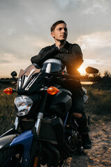 Fototapeta na wymiar Close-up photo of handsome biker sitting on motorcycle in sunset on the country road.