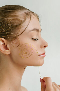Closeup profile portrait of a cute blond girl with closed eyes and the curl wire in her hand ner the cheek and curls from the hair