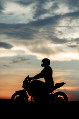 Silhouette photo of biker driving motorcycle in sunset on the on country road.