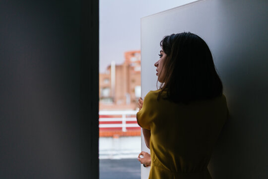 Young pretty woman standing at opened door looking outside