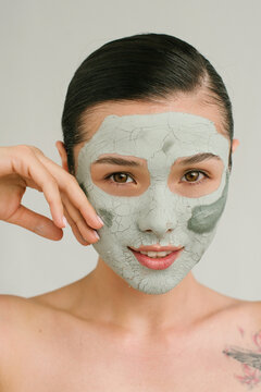 Closeup portrait of a charming Asian girl with a clay mask on her face and palm near the cheek