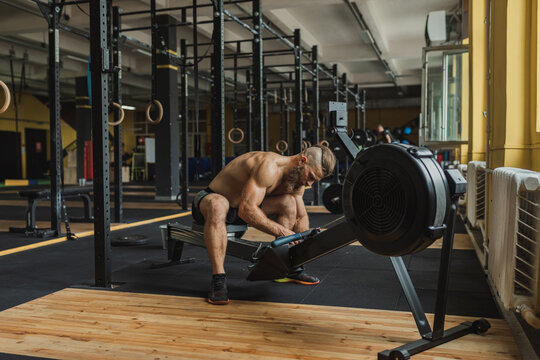Strong and healthy man working out on a rowing machine, inside a crossfit gym. - Powered by Adobe