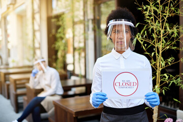 African American waitress with closed sing at sidewalk cafe during coronavirus epidemic.