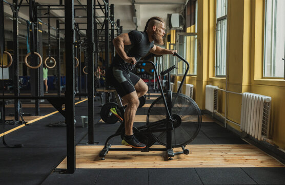 Strong and healthy man working out on a air bike, inside a crossfit gym.