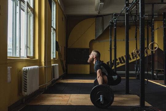 Strong and healthy man workin out with bar and weights inside a crossfit gym.
