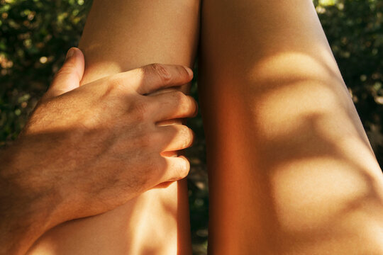 man's hand touching woman's legs in the sun closeup