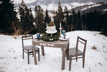 winter festive table for two person with delicious cake on the top of a mountain. delicious cake decorated with floristry.  Christmas tree wreath on a wooden table