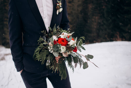 Beautiful winter bouquet in the hands of the groom. Groom holding bride's bouquet. dridal bouquet of roses with pine, branches of eucalyptus, succulents and pine cone in man's hands