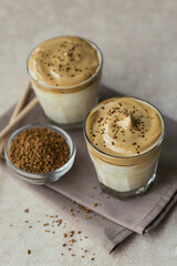 Glass of Iced Dalgona Coffee, trendy fluffy creamy whipped coffee and milk on light beige background.