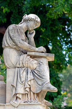Marble statue on the base of the statue of Ioannis Varvakis in the garden of the Zappeion Palace of Athens, with trees blurred in the backround
