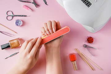 Woman does a manicure at home. Hands with a nail file on pink background. - obrazy, fototapety, plakaty