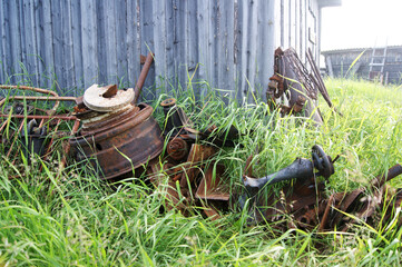 Fototapeta premium rusty scrap metal lies in the tall grass by the barn