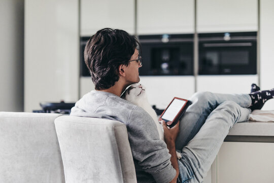 Guy sitting in the kitchen reading a book on his ereader with his cat on his lap