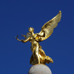 Fototapeta na wymiar Golden statue of Nike with a wreath in her hands on a background of blue sky