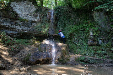 Fototapeta premium Black woman climbs to waterfall to reach out cool water in Switzerland.
