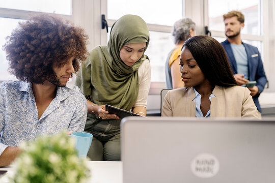 muslim woman in hijab, a african woman and curly hair man working together in the office using laptop.