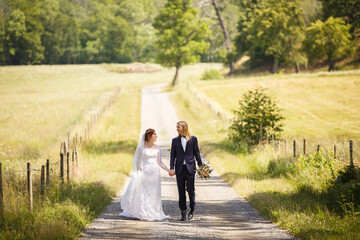 Fototapeta premium Young Bride and Groom couple in a summer garden. Tender holding each other. Redhead woman and blonde man with long hairs. Young family outdoor in nature. Love and tenderness