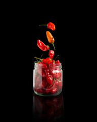 red sweet peppers falling into a glass jar in a Black background