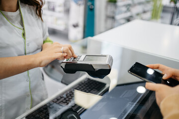 Detail of a client hands paying with the smartphone at a pharmacy